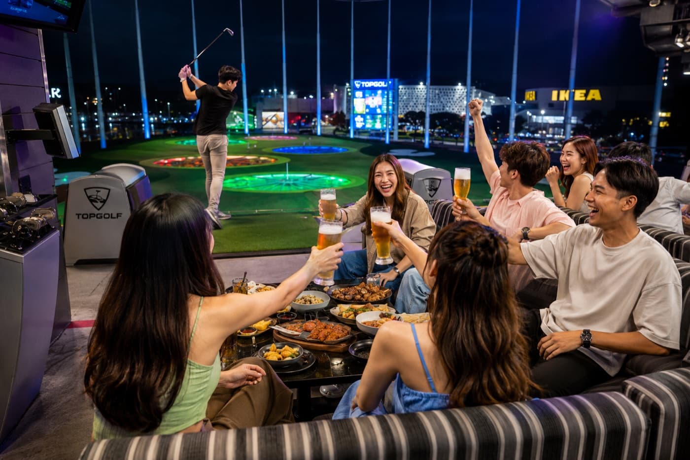 Friends clinking beer glasses beside the green at Topgolf